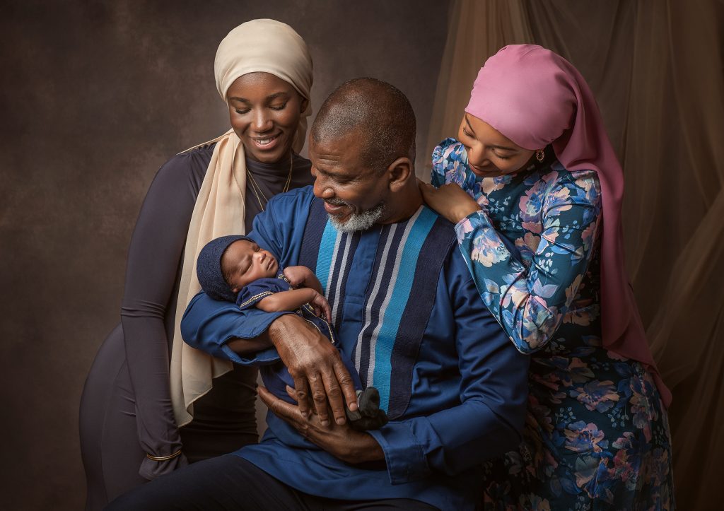 dark skin family and baby natural pose dad holds baby in his arms girls facing down the baby smiling studio shot in Sutton Surrey