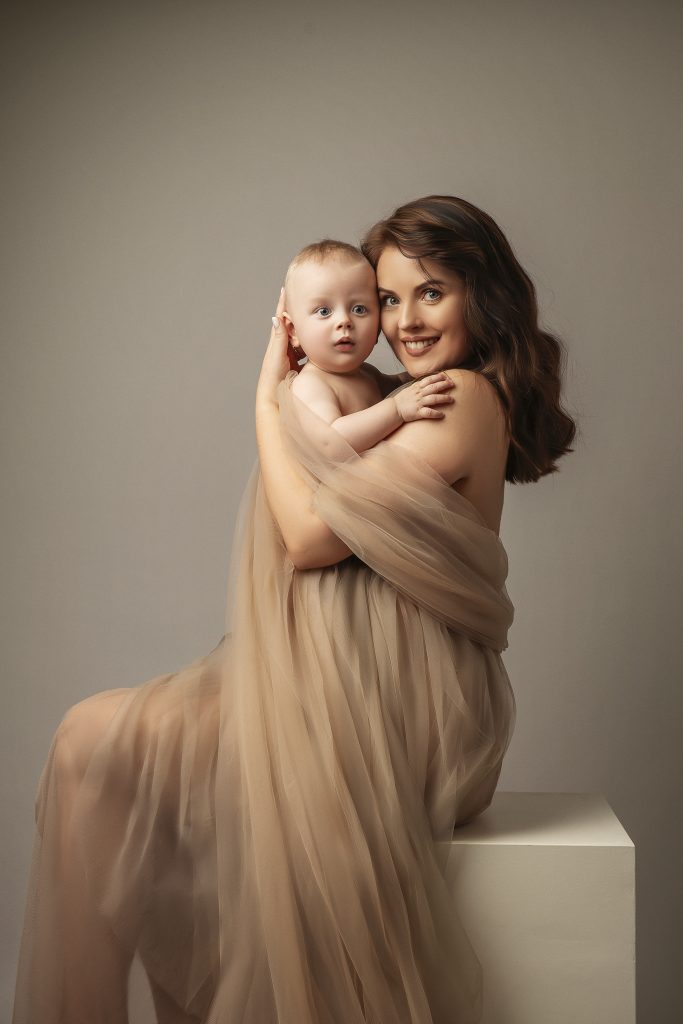 mum and baby boy wrapper in a natural tulle fabric creamy studio colours dreamy painterly mood facing the camera Sutton Surrey family photo