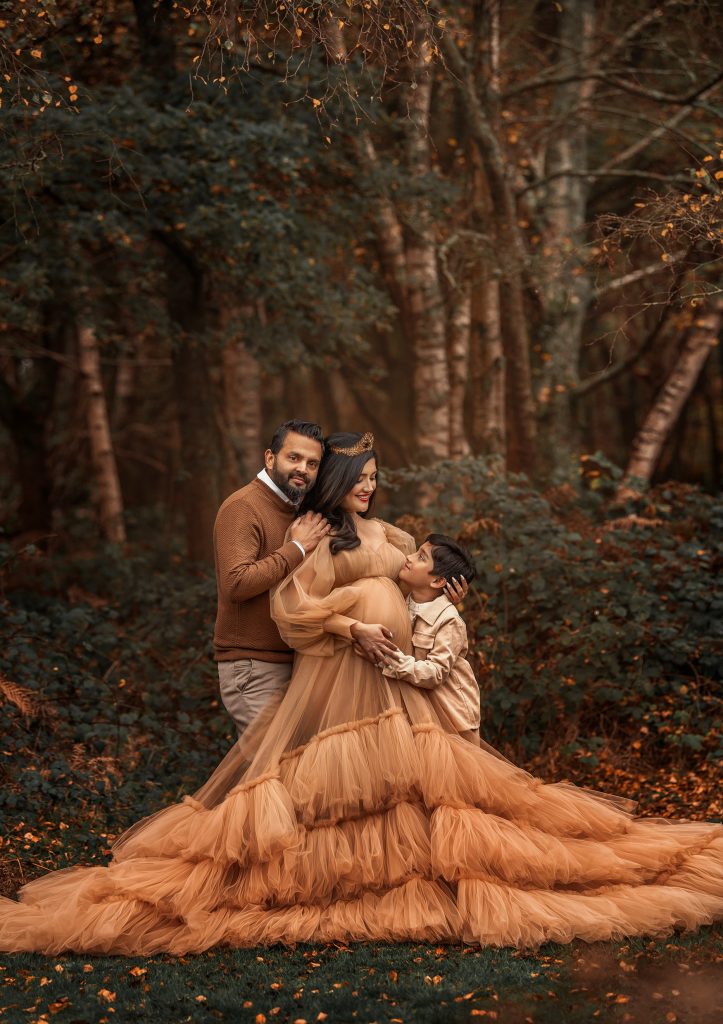 Family pregnancy photoshoot in the woods natural pose mum wearing long tulle creamy dress holding belly outdoors surroundings painterly mood Surrey