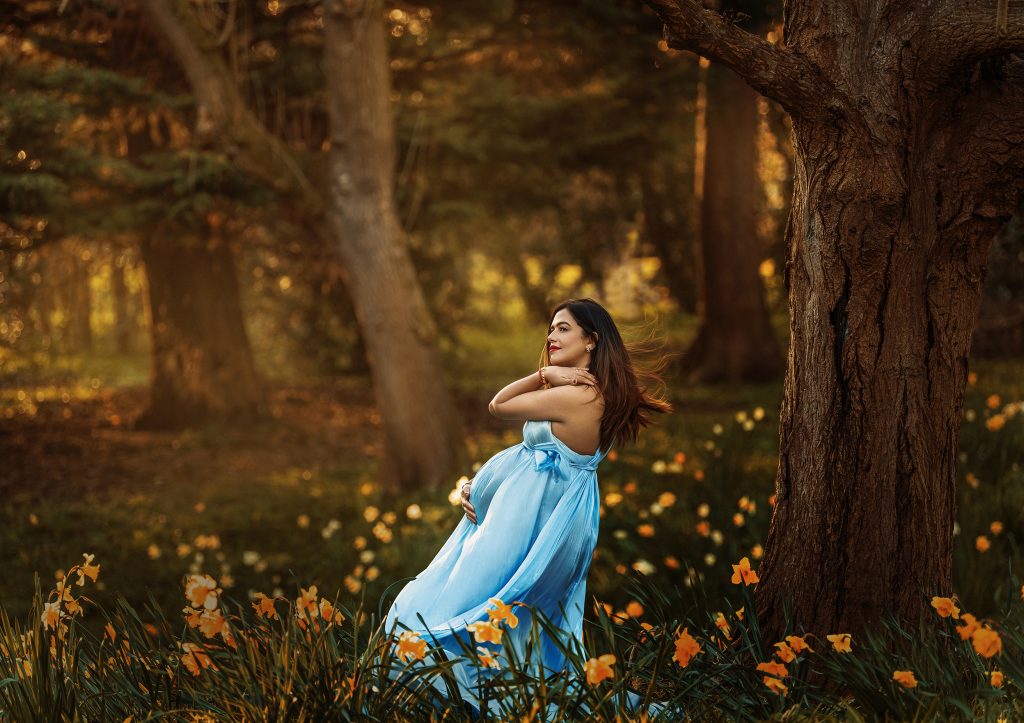 Nature inspired outdoors maternity painterly mood photography lady standing in the woods surrounded by trees and flowers dreamy maternity picture in Sutton Wimbledon Surrey and London