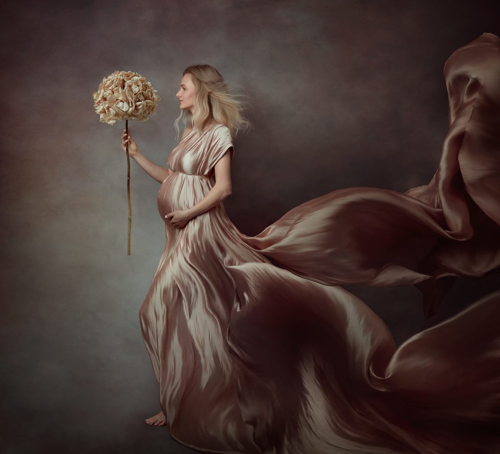 fine art painterly emotive pregnancy photography lady holding the belly and the flower flowing gown dreamy colours creative portrait in Sutton Surrey and London