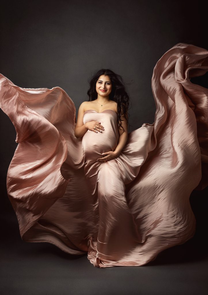 pregnant lady standing smiling holding belly rosy fabric flowing around her painterly timeless feminine photography in Sutton London Studio