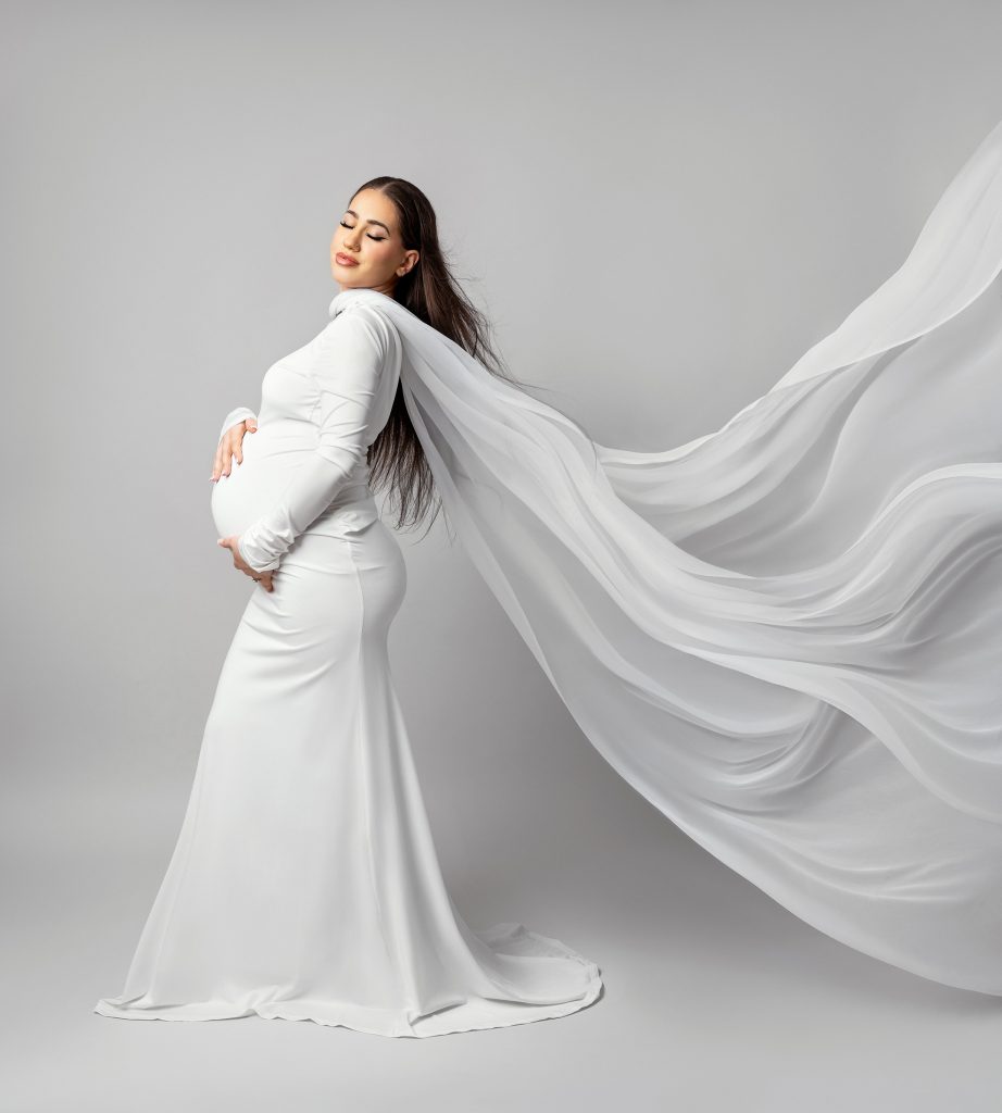 white styling white studio background long white dress maternity photo lady standing in classic pose hold belly dreamy mood studio in Sutton South London