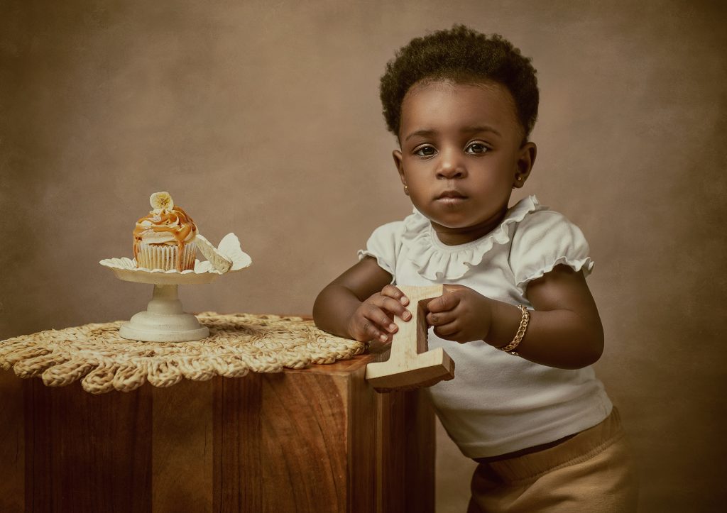 baby girl studio vintage mood first birthday photoshoot girl holding wooden number one and standing next to little cupcake Surrey South London photographer