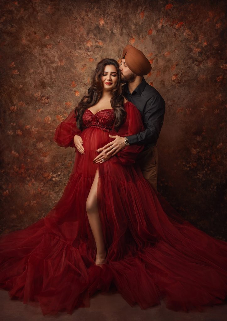 couple maternity studio photography lady wearing dark red tulle gown her husband holding her belly hugging connection captured dreamy painterly style photo taken in Sutton Surrey studio