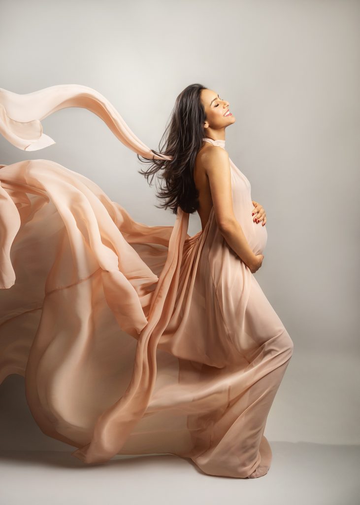 stylish natural elegant maternity shoot pregnant lady wearing long creamy flowy dress holding belly smiling with the eyes closed photography in Carshalton Sutton Surrey Wallington