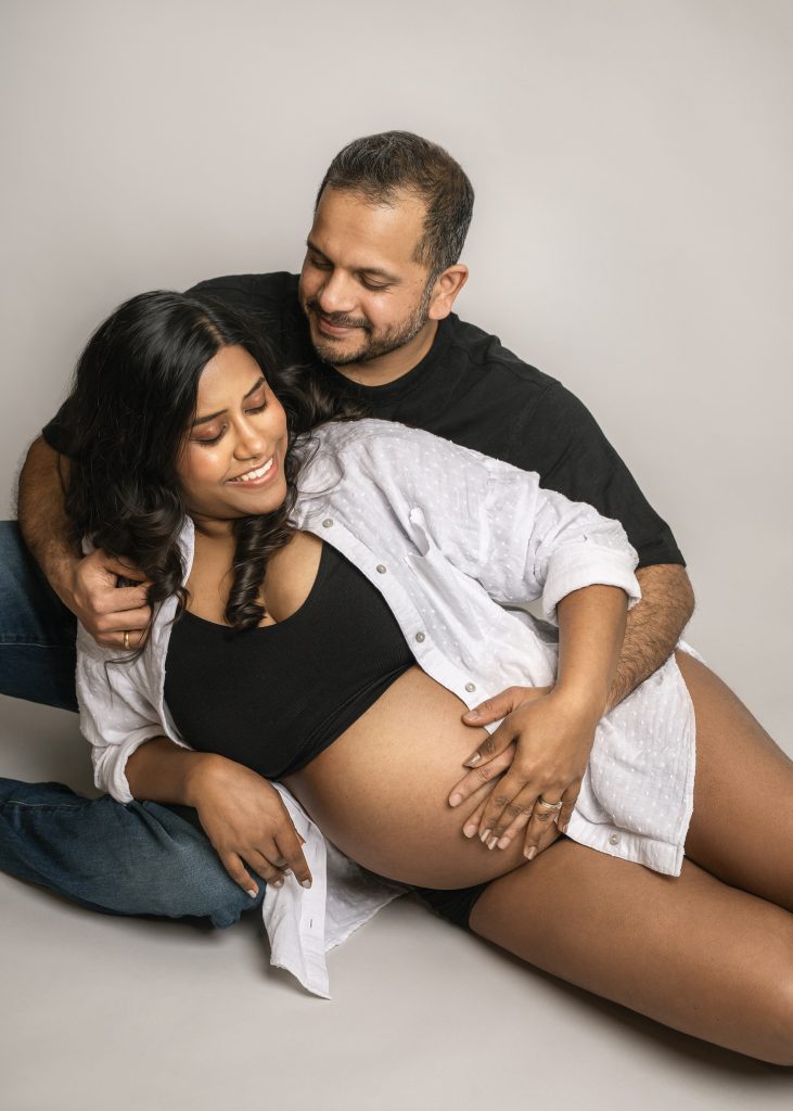 casual style couple maternity studio photoshoot couple sitting on the floor wearing white and black clothes smiling Sutton London Surrey photographer