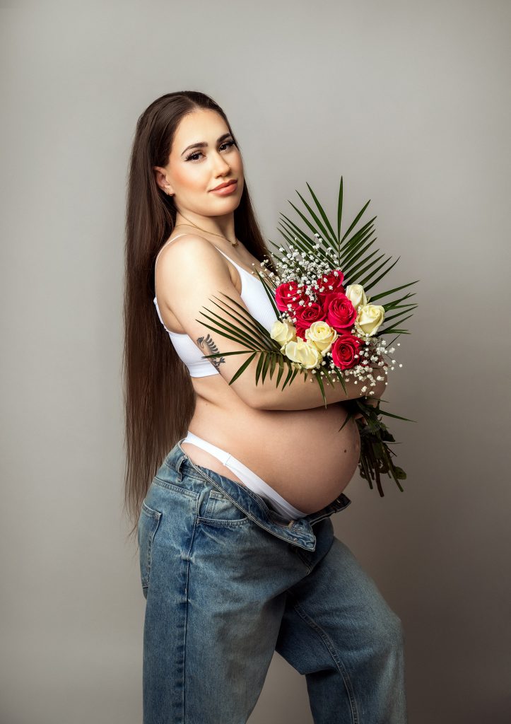 casual maternity studio portrait pregnant lady wearing jeans and crop top holding flowers shoot taken in Sutton London and Surrey