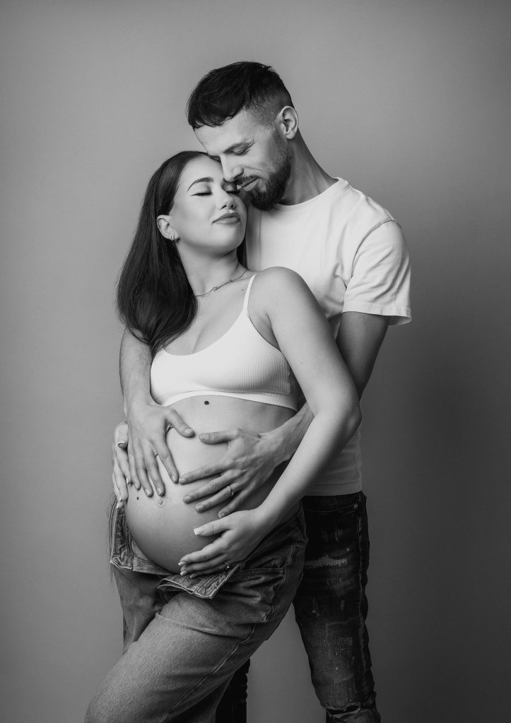 black and white couple pregnancy photoshoot casual style a couple hugging closed eyes holding belly together wearing jeans and white top maternity photoshoot in Sutton London and Surrey