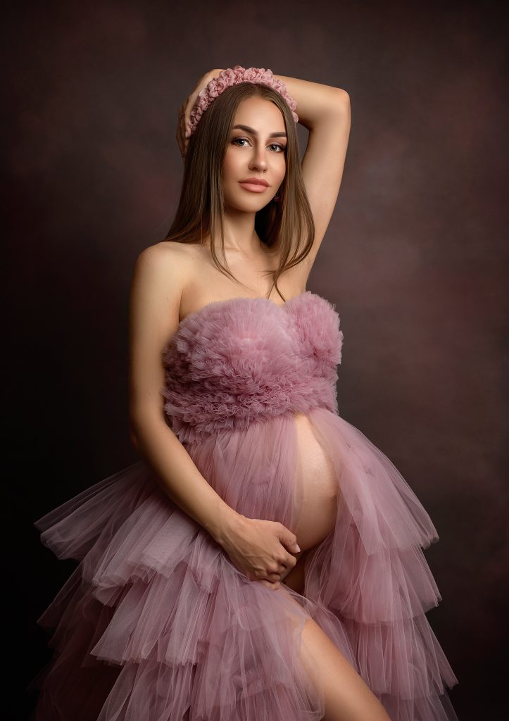 Classic dreamy studio maternity photo lady wearing pink ruffled dress and matching headband hold belly in a feminine pose Sutton Surrey photographer