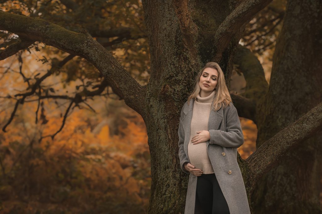 natural autumn casual maternity photo in woods surroundings pregnant lady leaning on the big tree closed eyes dreamy mood holding belly Purley pregnancy photoshoot