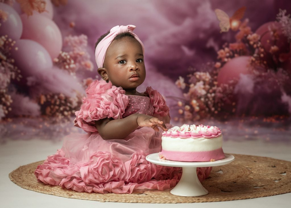 baby girl studio cake smash first birthday photo pink dress black skin baby girl floral backdrop Sutton Surrey