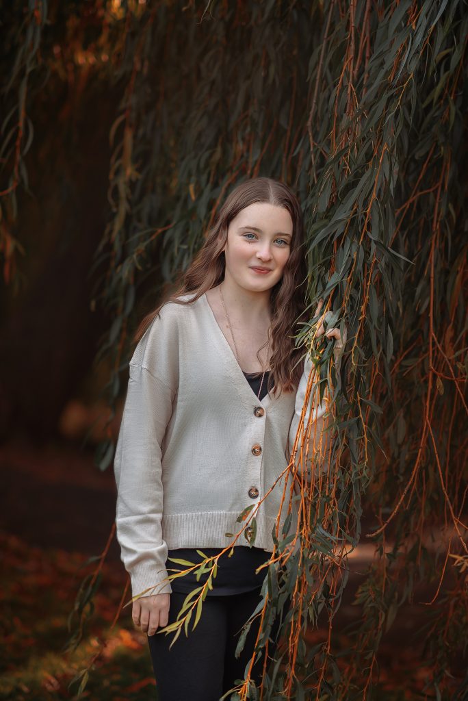 natural relaxed teenager girl portrait at Beddington park, Wallington she stands looks and smiles to the camera wears casual clothes, holds a branche of a tree