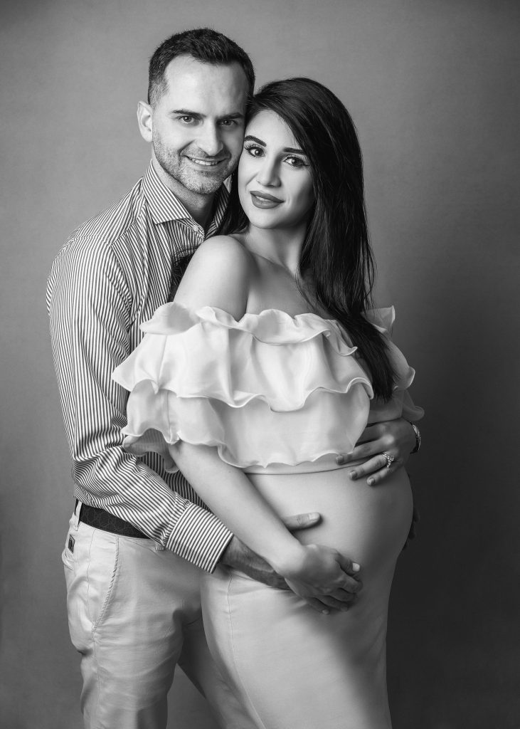 black and white studio natural casual pregnancy photo couple standing holding belly smiling to the camera timelles classic pregnancy Sutton Surrey