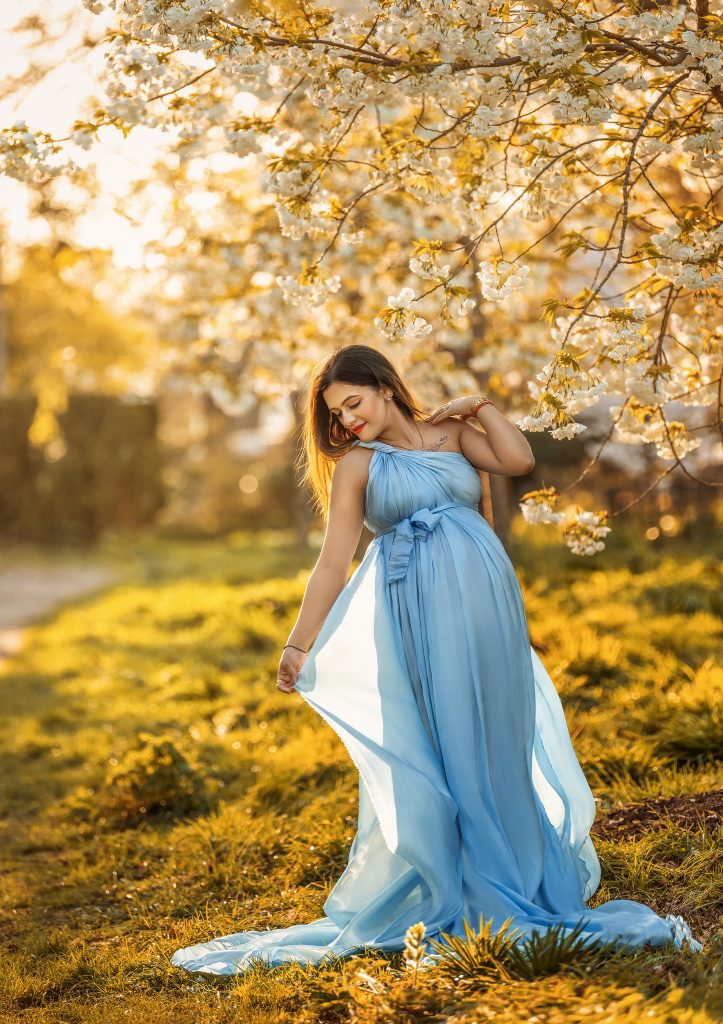 cherry blossom maternity dreamy romantic photo pregnant lady flows the blue fabric dress around her Surrey Sutton photoshoot