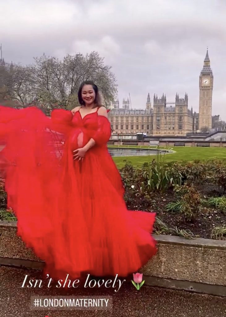 pregnant lady back stage from maternity photoshoot in London famous spot wearing red tulle long dress smiling at the camera