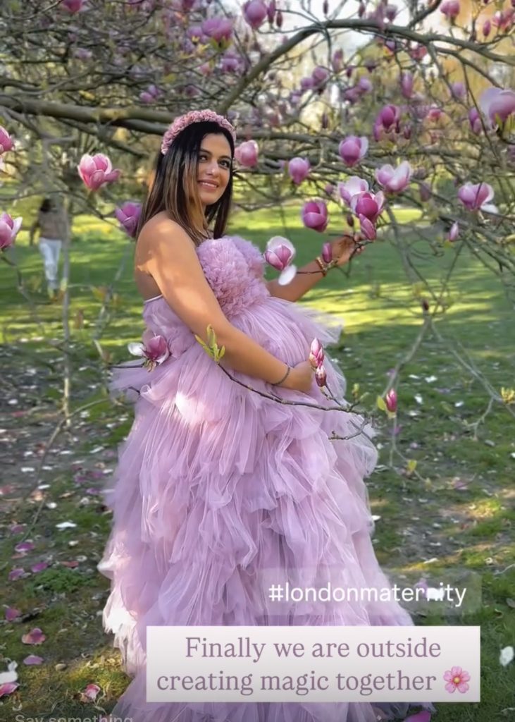 pregnancy back stage screenshot at the London park lady holding belly smiling and relaxed mood wearing long pink ruffled dress