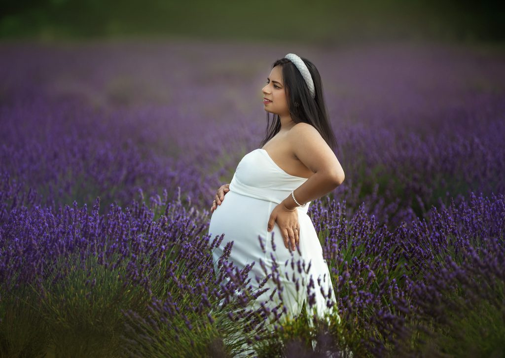 maternity photo taken in Summer at Mayfield Lavender field pregnant lady posing on the side holding belly wearing white gown
