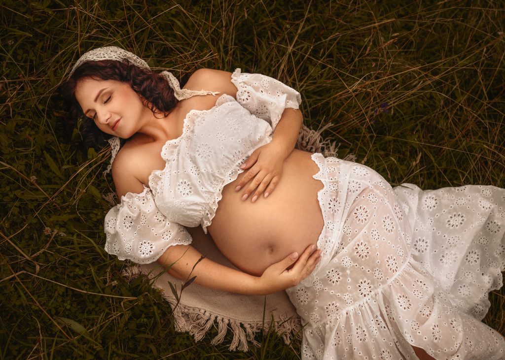 pregnant lady laying in the grass boho style maternity photoshoot in nature natural white outfit Surrey photographer