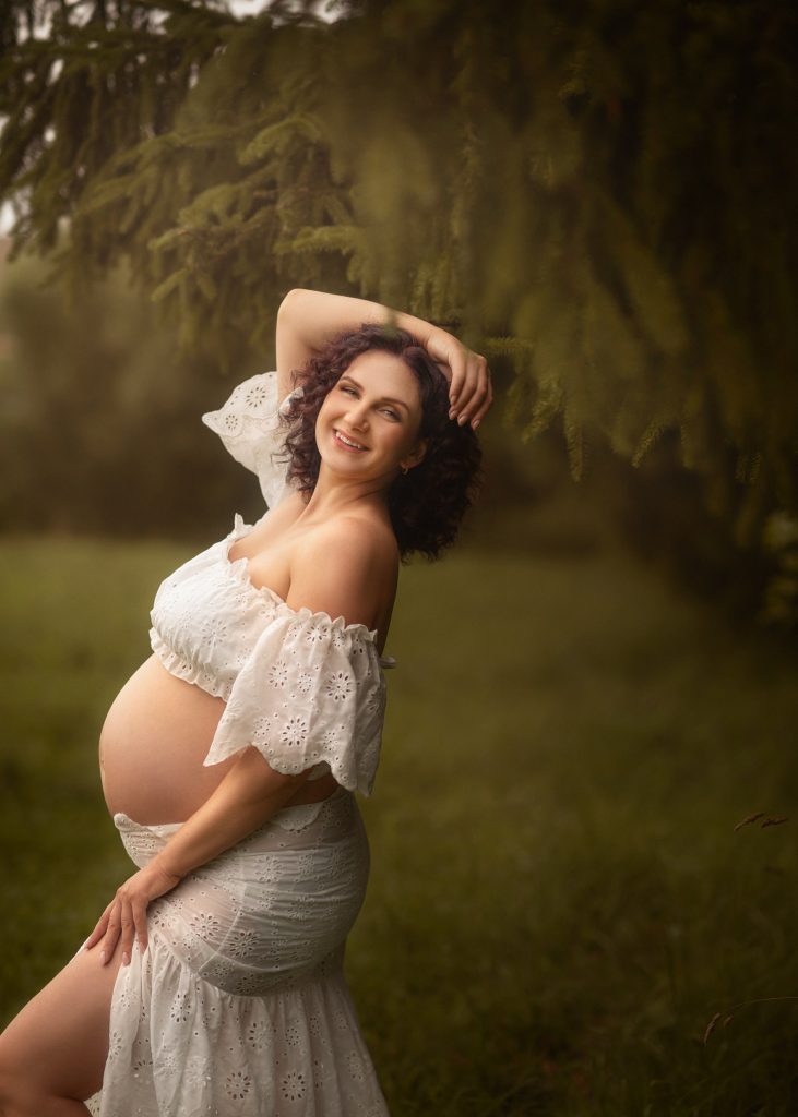 pregnant lady posing in natural woodlands background smiling at the camera wearing white outfit Surrey photoshoot